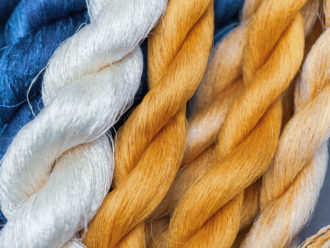A series of different colored threads starting at the left with a deep blue then white and then a golden yellow