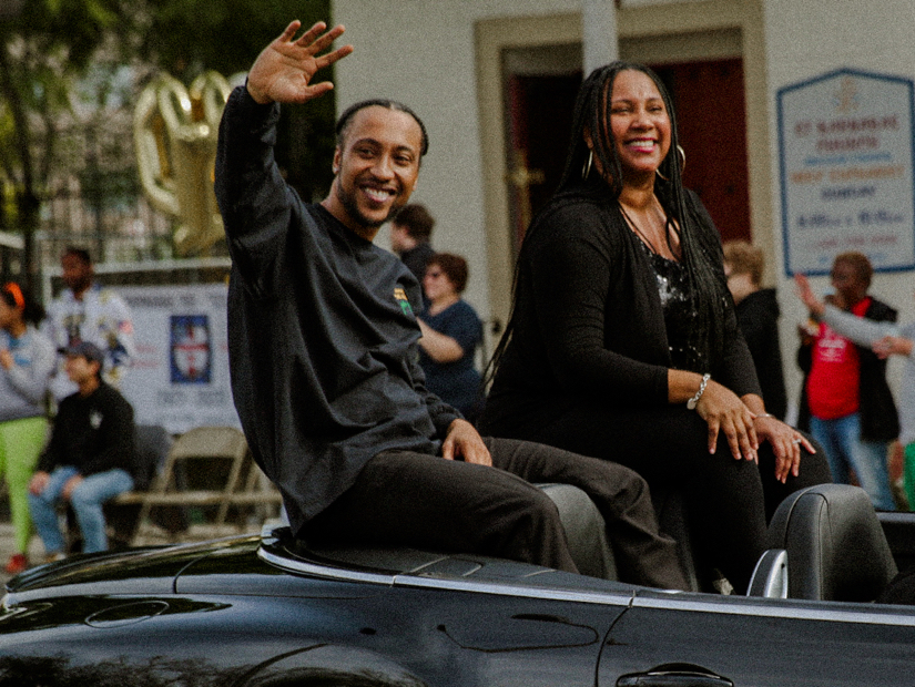 Two people sitting in a car at the Black History Parade and waving at the crowd
