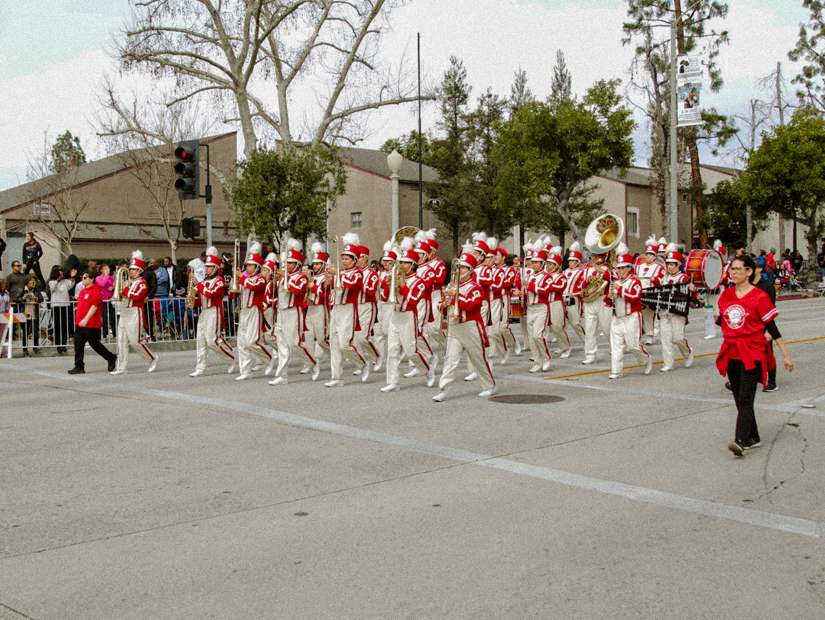 A marching band dressed in red and white playing their instruments and walking down the street at the Black History Parade