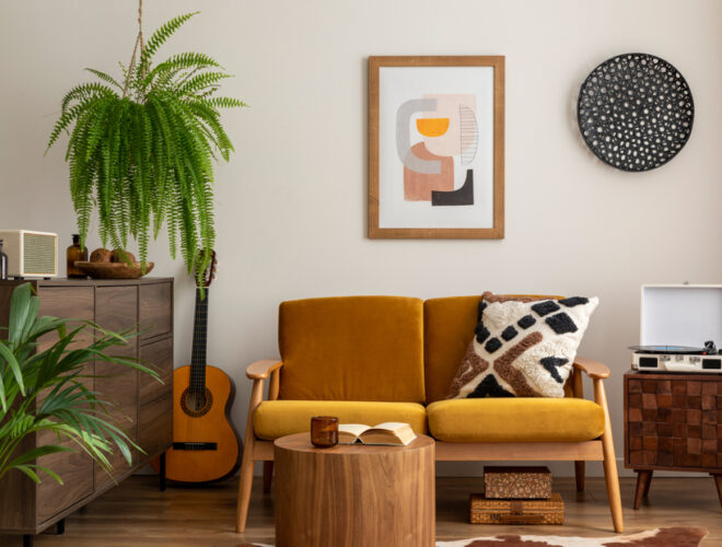 A living room with an orangish brown couch with a painting hung in the background. Beside the couch is a large green potted plant.